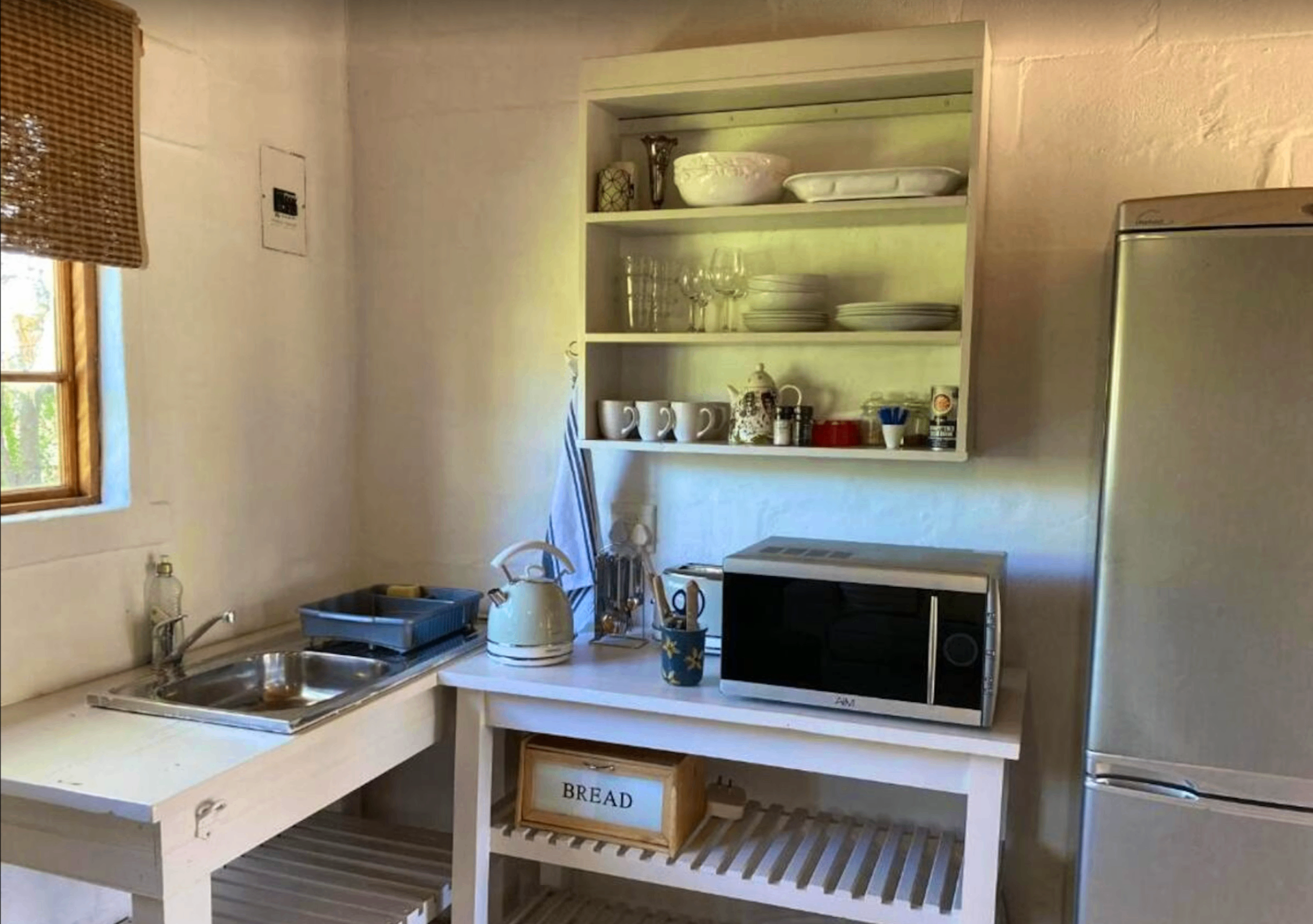 Kitchenette at Karoo Feels with open shelving, crockery, microwave, kettle, and fridge.