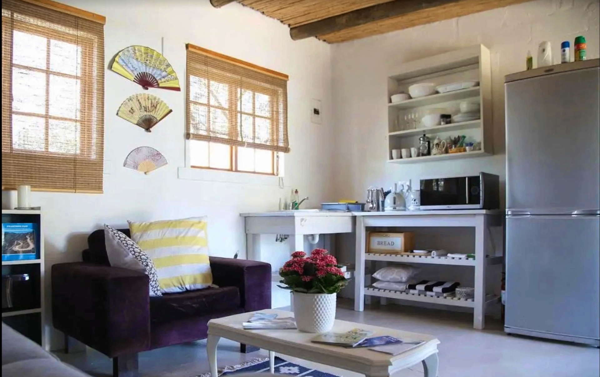 Open-plan lounge and living space at the cottage with sofa, armchair, coffee table, and kitchenette beyond.