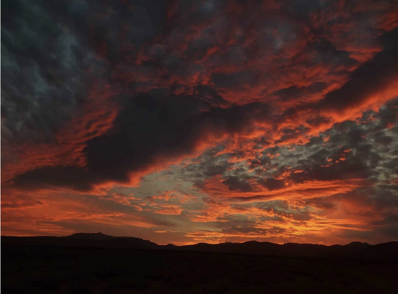 Fiery Karoo sunset with red-orange clouds above mountain silhouettes.